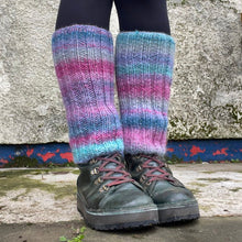 Load image into Gallery viewer, Person wearing colourful striped knee-high leg warmers and dark shoes against a textured wall.