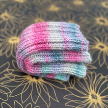 Load image into Gallery viewer, stack of colourful folded leg warmers on a floral background