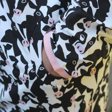 Load image into Gallery viewer, A close-up of a hand in a pocket in a black and white cow print fabric with pink accents, featuring a pink binding on the cuff