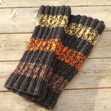 Load image into Gallery viewer, A pair of hand-knit wool leg warmers with a striped pattern of black, orange, brown, and gold, displayed on a rustic wooden table