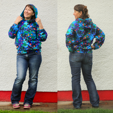 Load image into Gallery viewer, A woman modeling a colorful abstract patterned hoodie with blue jeans, shown in a side-by-side front and back view against a white stucco wall with a red painted base.
