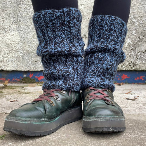 Person wearing dark green boots with knitted leg warmers against a concrete wall.
