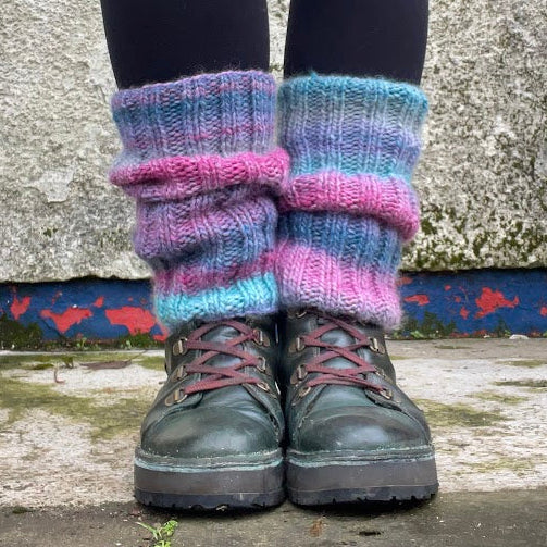 Person wearing colorful leg warmers and dark boots against a textured wall.