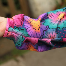 Load image into Gallery viewer, A close-up of a sleeve featuring a vibrant, multicolored floral pattern with pink, purple, teal, and orange flowers, worn by a person whose hand is visible on the left.
