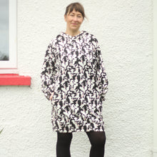 Load image into Gallery viewer, A woman wearing a black and white print hooded sweatshirt dress and black tights, standing in front of a white textured wall
