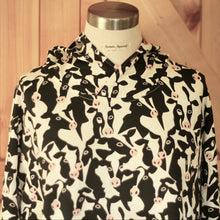 Load image into Gallery viewer, A hooded long-sleeve shirtdress with an all-over cow print, displayed on a mannequin torso against a wooden background.
