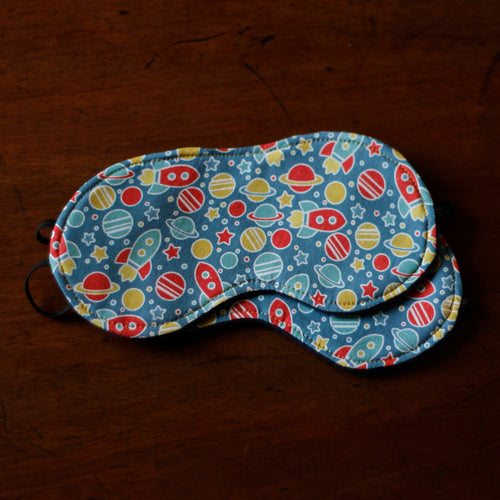 Sleep mask with space-themed pattern on a dark brown surface