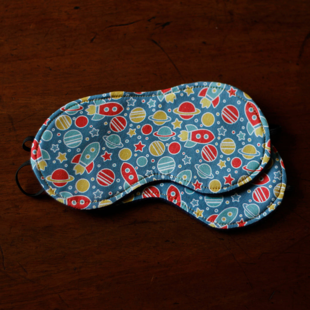 Sleep mask with space-themed pattern on a dark brown surface