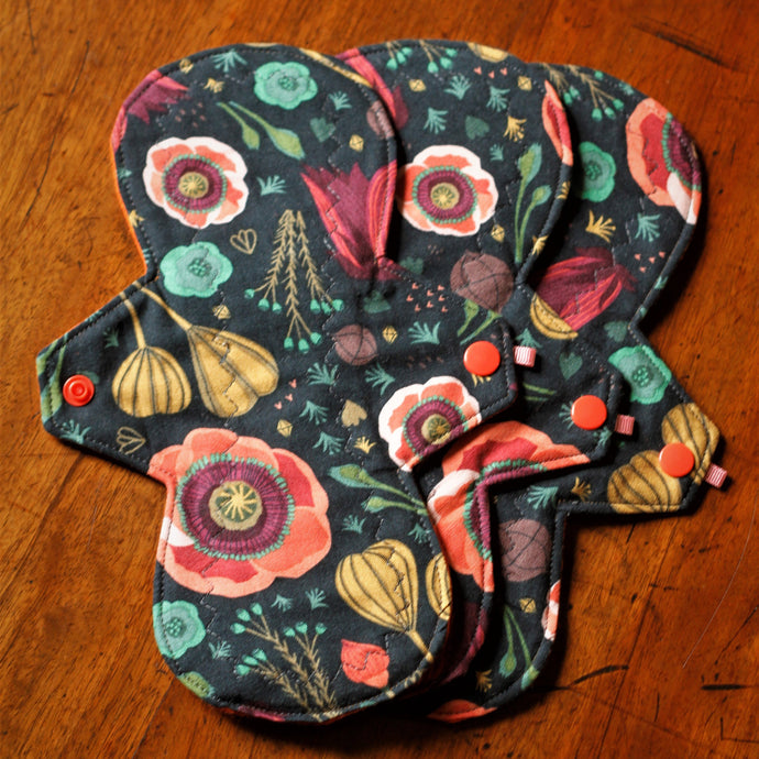 The dark blooms is a black background pad with poppy seedheads and flowerheads