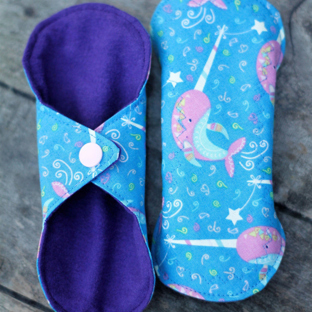 The narwal pattern is a bright sky blue pad with pink narwals on the top layer and a plain purple flannel bottom layer